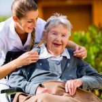 Senior women at home with nurse in garden sitting in wheelchair