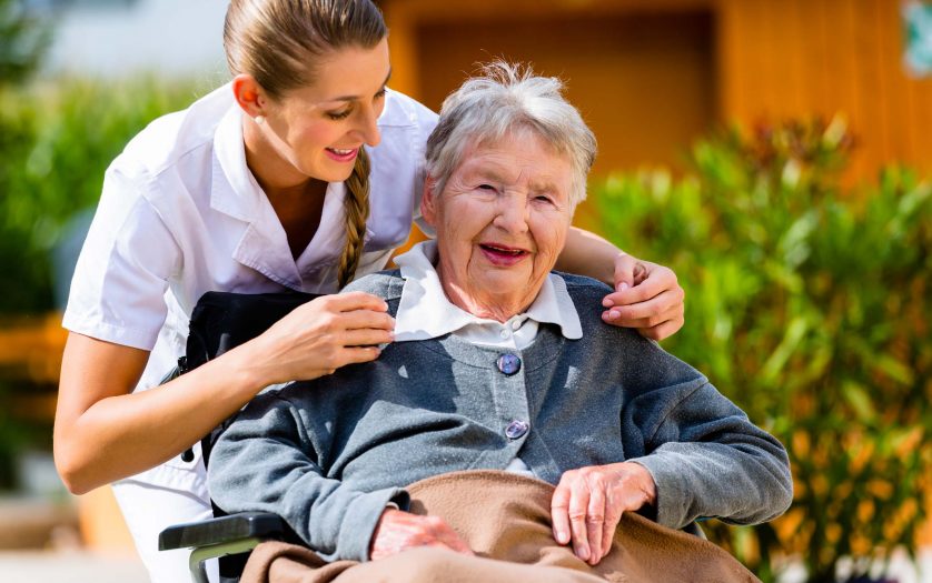 Senior women at home with nurse in garden sitting in wheelchair