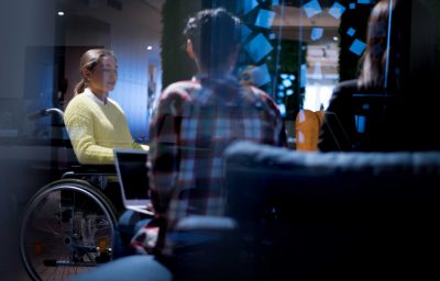 young woman in wheelchair with colleagues working in office