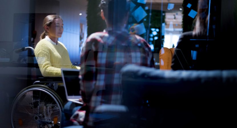 young woman in wheelchair with colleagues working in office