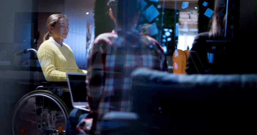 young woman in wheelchair with colleagues working in office