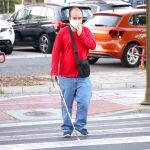Blind person with white stick walking on street and crossing a crosswalk.