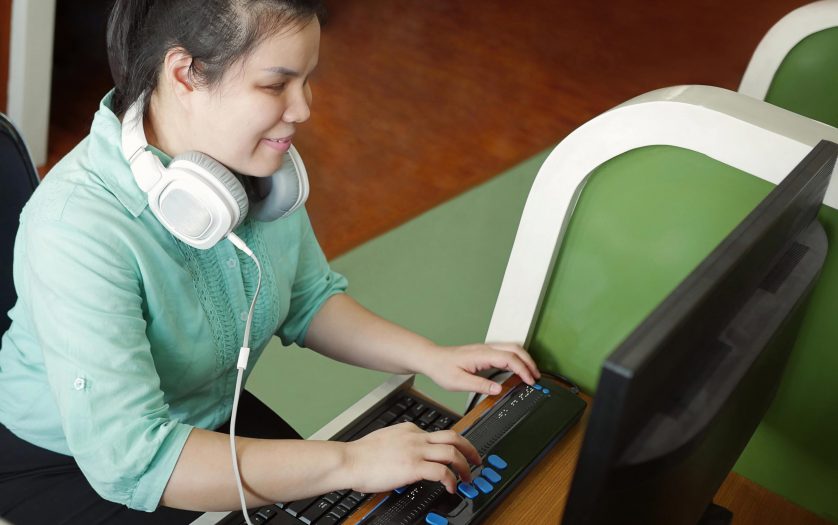 young blind woman with headphone using computer with refreshable braille display
