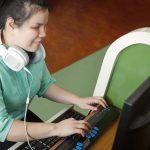young blind woman with headphone using computer with refreshable braille display or braille terminal a technology device for persons with visual disabilities.