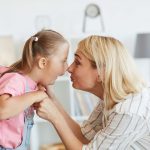 Girl with down syndrome and her mother looking at each other face to face they playing at home