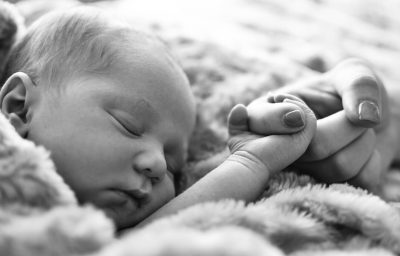 New born baby sleeping while holding mothers finger