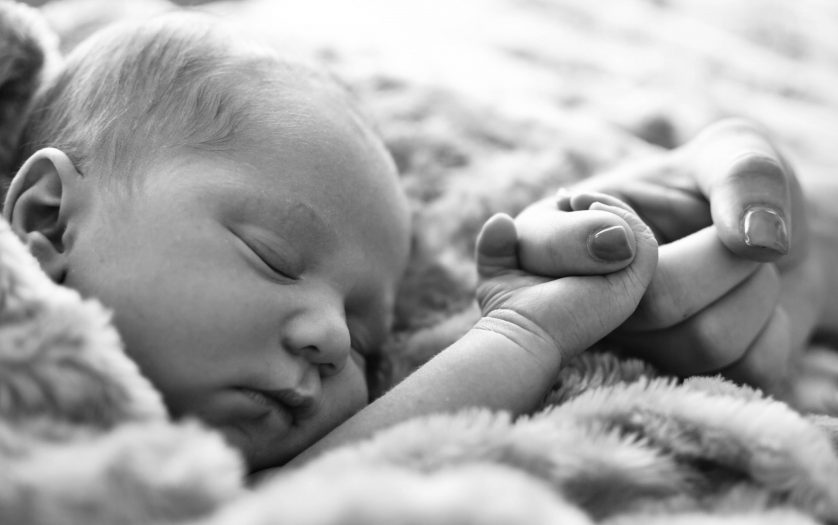 New born baby sleeping while holding mothers finger