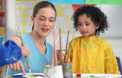 Young teacher assisting cute girl in painting during art class