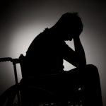 Sad man sitting on wheelchair in empty room