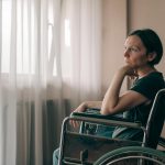 woman in worn wheelchair looking out the window and thinking