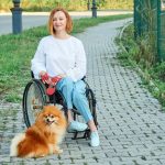 A woman in a wheelchair walks with her dog outdoor.