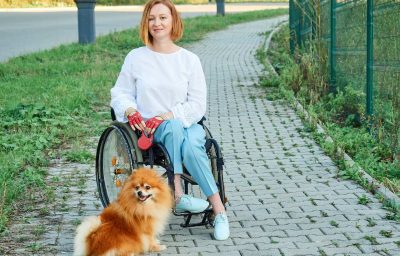 A woman in a wheelchair walks with her dog outdoor.