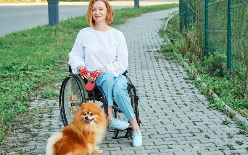 A woman in a wheelchair walks with her dog outdoor.
