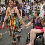 A woman walking together with her partner in wheelchair at the Pride parade