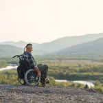 young man in a wheelchair enjoying fresh air in sunny day on the mountain
