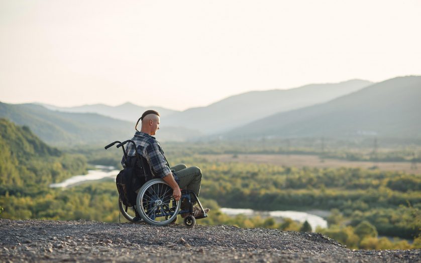 young man in a wheelchair enjoying fresh air in sunny day on the mountain