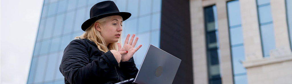 Young woman speaks sign language on a video call on a laptop outdoor.