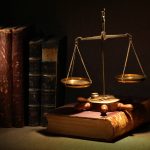Legislation concept. Old brass weight scale and ancient books under beam of light on dark background