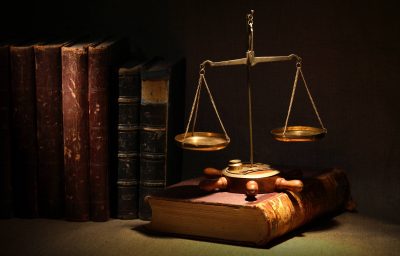 Legislation concept. Old brass weight scale and ancient books under beam of light on dark background