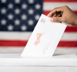 Concept of Mail in vote at US election - hands dropping mail inside the ballot box with us flag as background