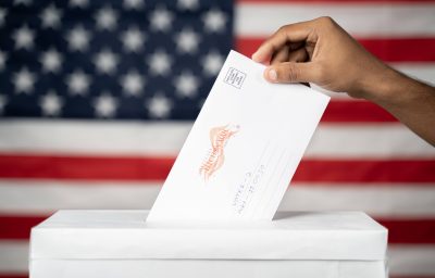 Concept of Mail in vote at US election - hands dropping mail inside the ballot box with us flag as background