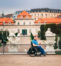 man tourist in wheelchair traveling in Europe. Lower Belvedere at background, Vienna, Austria