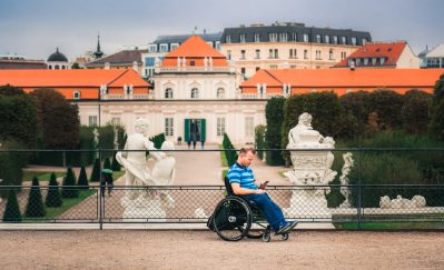 man tourist in wheelchair traveling in Europe. Lower Belvedere at background, Vienna, Austria