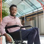Portrait of African young disabled man sitting in wheelchair at office building