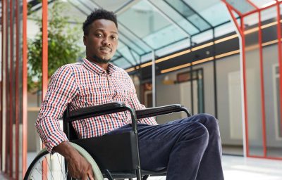 Portrait of African young disabled man sitting in wheelchair at office building