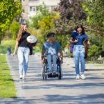 man in wheelchair spending time with friends playing live instrumental music outdoors