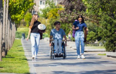 man in wheelchair spending time with friends playing live instrumental music outdoors