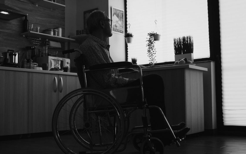 Silhouette of man in wheelchair feeling lonely looking on the window
