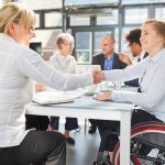 Businesswoman and colleague in a wheelchair handshaking in a business meeting