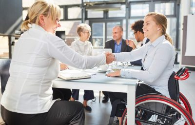 Businesswoman and colleague in a wheelchair handshaking in a business meeting