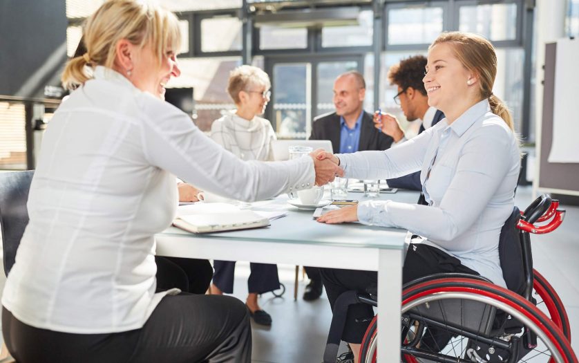 Businesswoman and colleague in a wheelchair handshaking in a business meeting