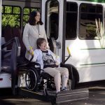 A woman in a wheelchair is helped off a van using a chair lift.