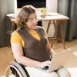 Young woman in wheelchair using computer at home