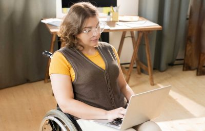 Young woman in wheelchair using computer at home