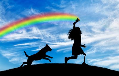 Child has a disability with a prosthetic leg with a brush in hand runs and draws a rainbow in sky with his dog