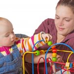 Baby with motor activity development delay being stimulated to develop muscle coordination and movement on a bead maze watched by a mother