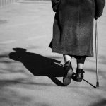 On a sunny day a old woman walking down the street with walking stick