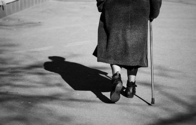 On a sunny day a old woman walking down the street with walking stick