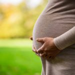 Close-up of pregnant woman who is holding her stomach in park.