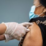 Doctor in gloves holding syringe and making injection to woman