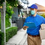 delivery man in blue t-shirt carrying parcel box and document to sign in front of customer home.