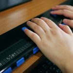 Close-up blind person hands using computer with braille display