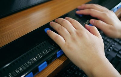 Close-up blind person hands using computer with braille display