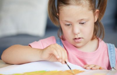 Child with down syndrome painting with paintbrush at the table at home