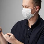 Young man with medical face mask measuring blood sugar level.