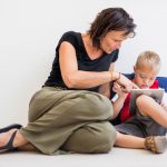 down-syndrome school boy sitting on the floor with mother, using tablet.